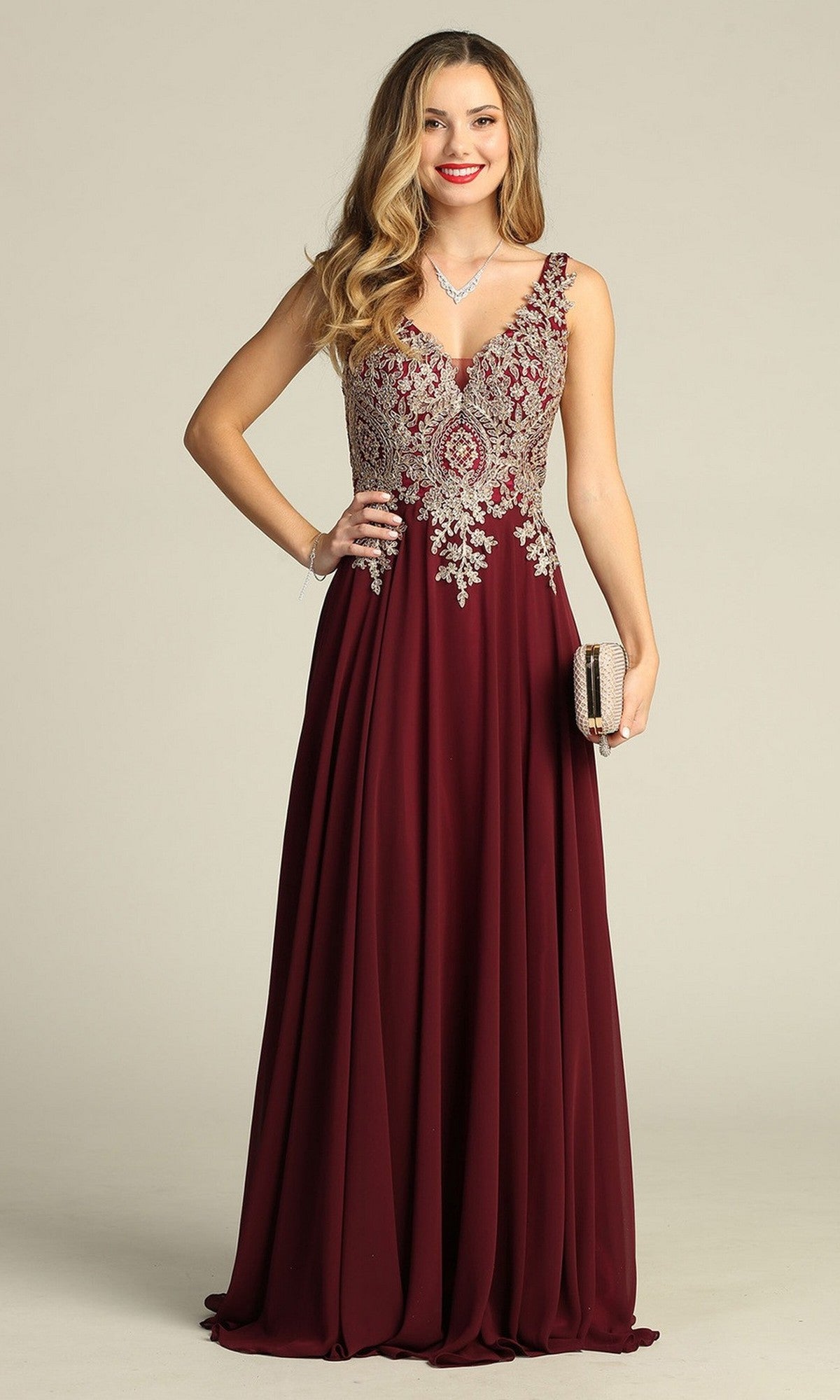 A woman stands smiling against a plain background, holding a small clutch purse while wearing the Long Formal Dress: Chicas DM4006 in plum—a sleeveless gown featuring an embroidered bodice and a flowing chiffon A-line skirt.